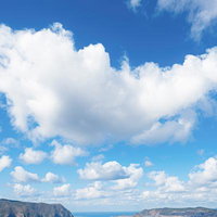 島と青空と白い雲が映る海辺の風景、山々が連なる自然景観の写真