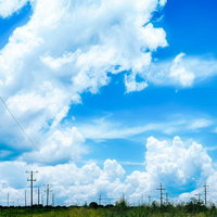 送電線と真夏日の積乱雲が立ち込める田園風景の写真
