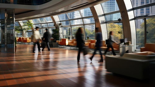 高層オフィスビルのガラス張りロビーを往来するビジネスパーソン