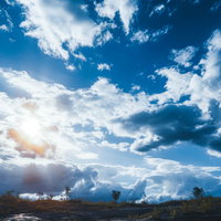 日中の雲が浮かぶ青空と原っぱの日の入り風景の写真