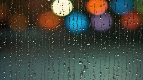 ネオンのひかりが映るガラス窓に流れる水滴