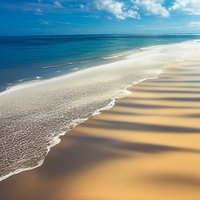 どこまでも続く南国の波打ち際と白い砂浜、青い海の写真