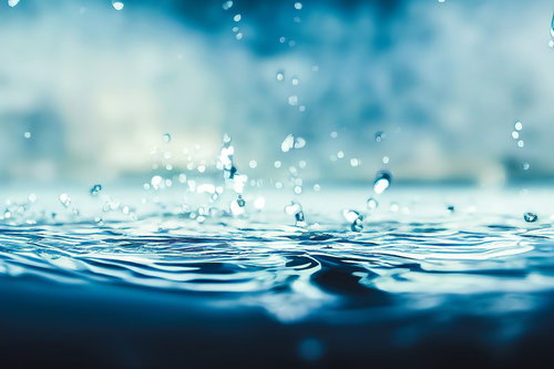 青い水面に落ちる透明な水滴と波紋が広がる瞬間