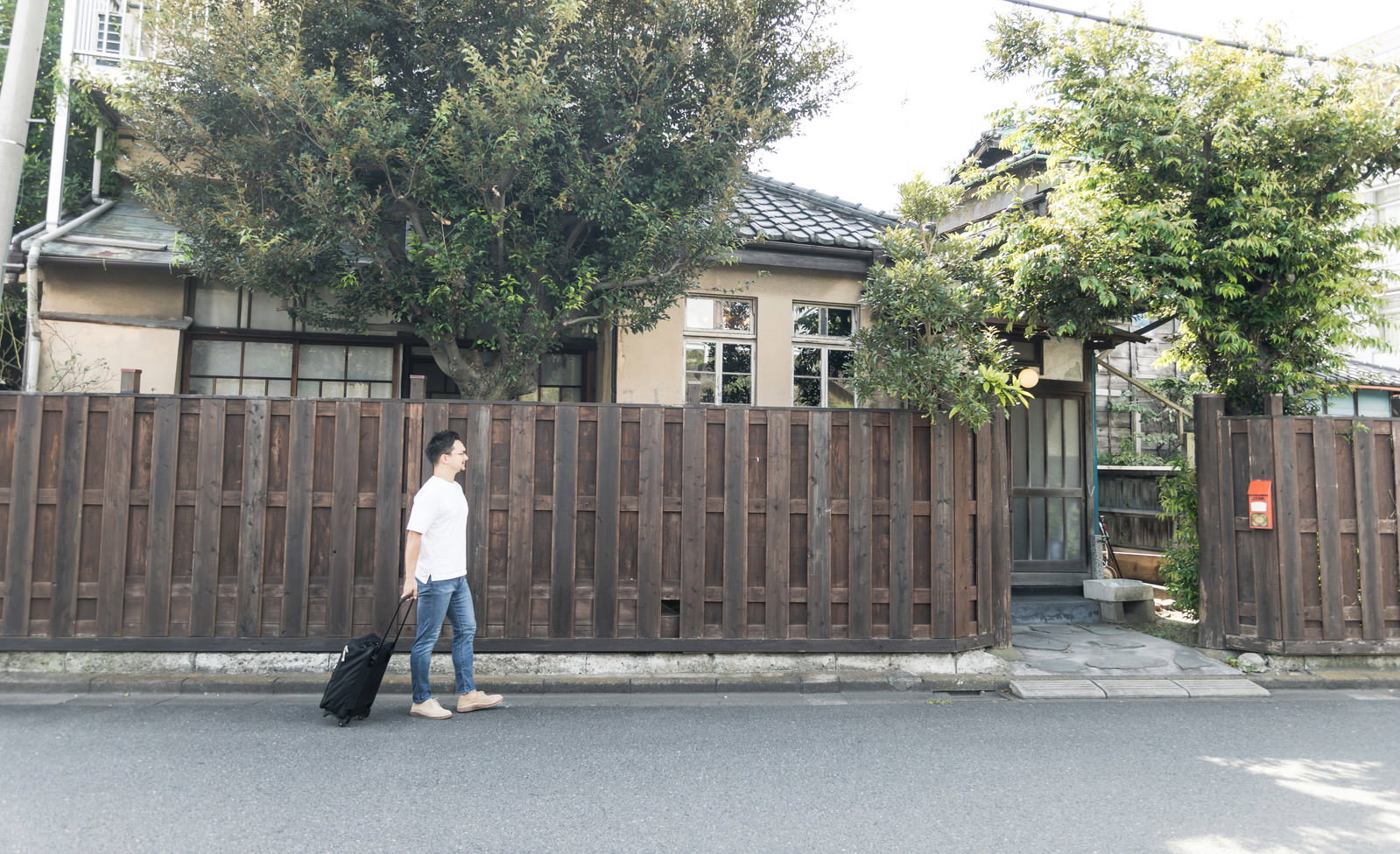 古民家の前でキャリーケースを引いて歩く外国人観光客の男性［モデル：Max_Ezaki］