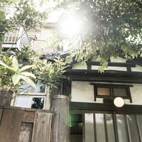 古民家の玄関前に差し込む木漏れ日と緑の植物の写真