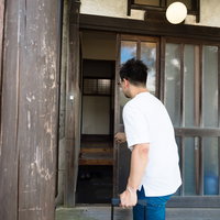 古民家の木製玄関引き戸を開ける男性の写真