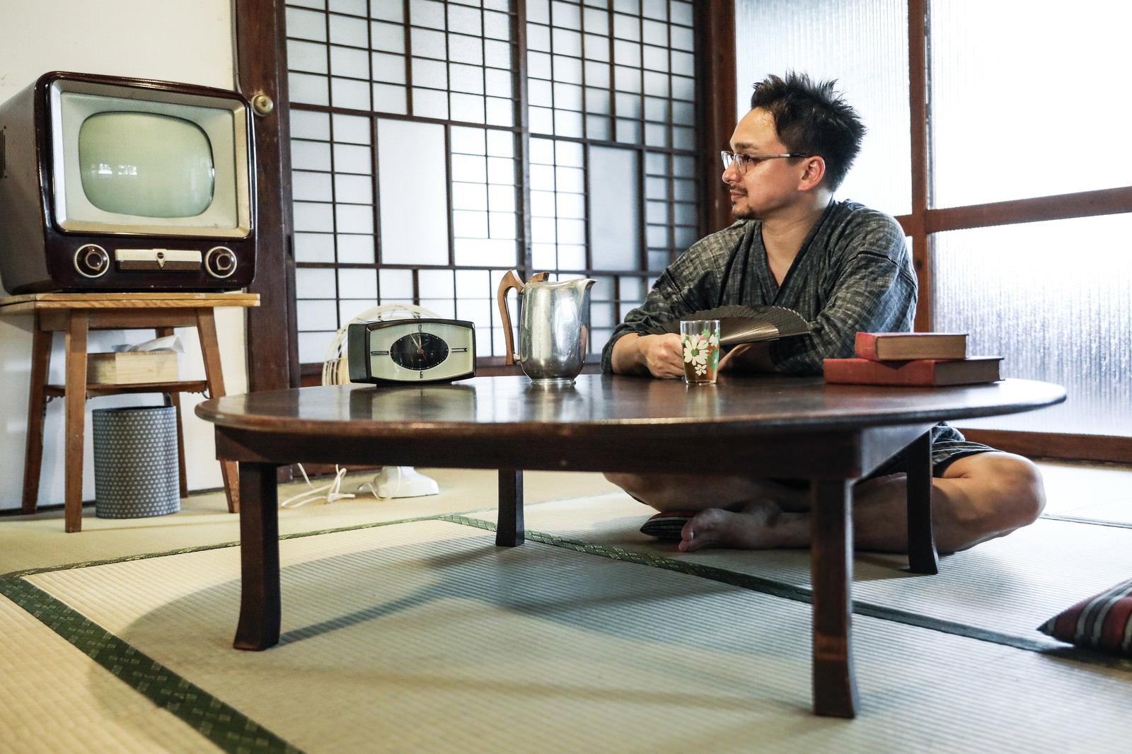 畳の和室でちゃぶ台とアナログテレビがある空間で甚平を着た外国人男性がくつろいでいる［モデル：Max_Ezaki］