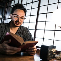 古民家の書室で障子の光を受けながら本を読む外国人男性の写真