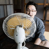 古民家で扇風機の風を浴びる甚平姿の男性が座卓で涼むの写真