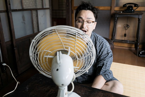 古民家で扇風機の風を浴びる甚平姿の男性が座卓で涼む