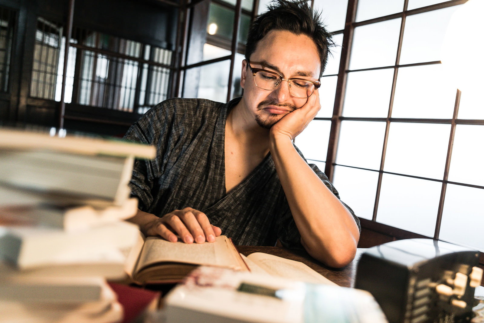 古民家の和室で畳の上に本を積み重ね、頬杖をついて読書する男性［モデル：Max_Ezaki］