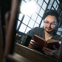 古民家の格子窓で読書に勤しむ眼鏡をかけた外国人男性の写真
