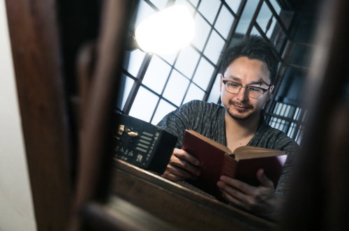 古民家の格子窓で読書に勤しむ眼鏡をかけた外国人男性