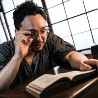 古民家で読書しながら調べ物をする眼鏡をかけた若い外国人男性の写真