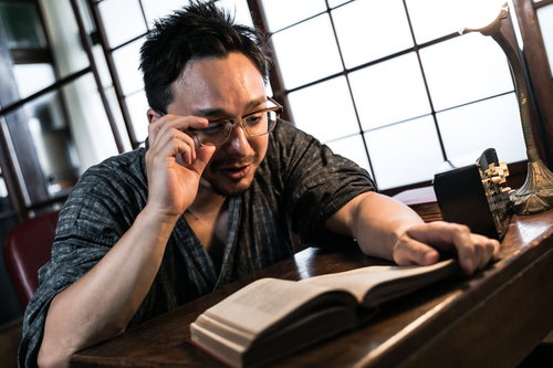 古民家で読書しながら調べ物をする眼鏡をかけた若い外国人男性
