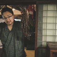 古民家の玄関に立つ甚平姿の外国人男性とじゃらじゃらのれんの写真