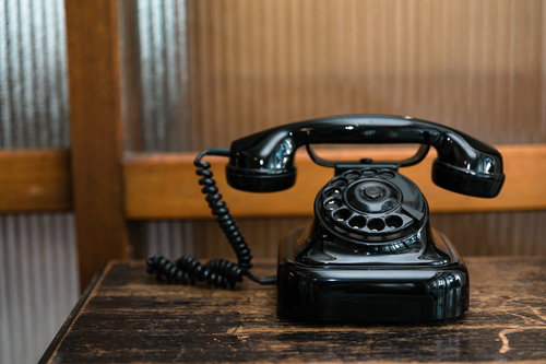 木製テーブルの上に置かれたダイヤル式の黒電話機