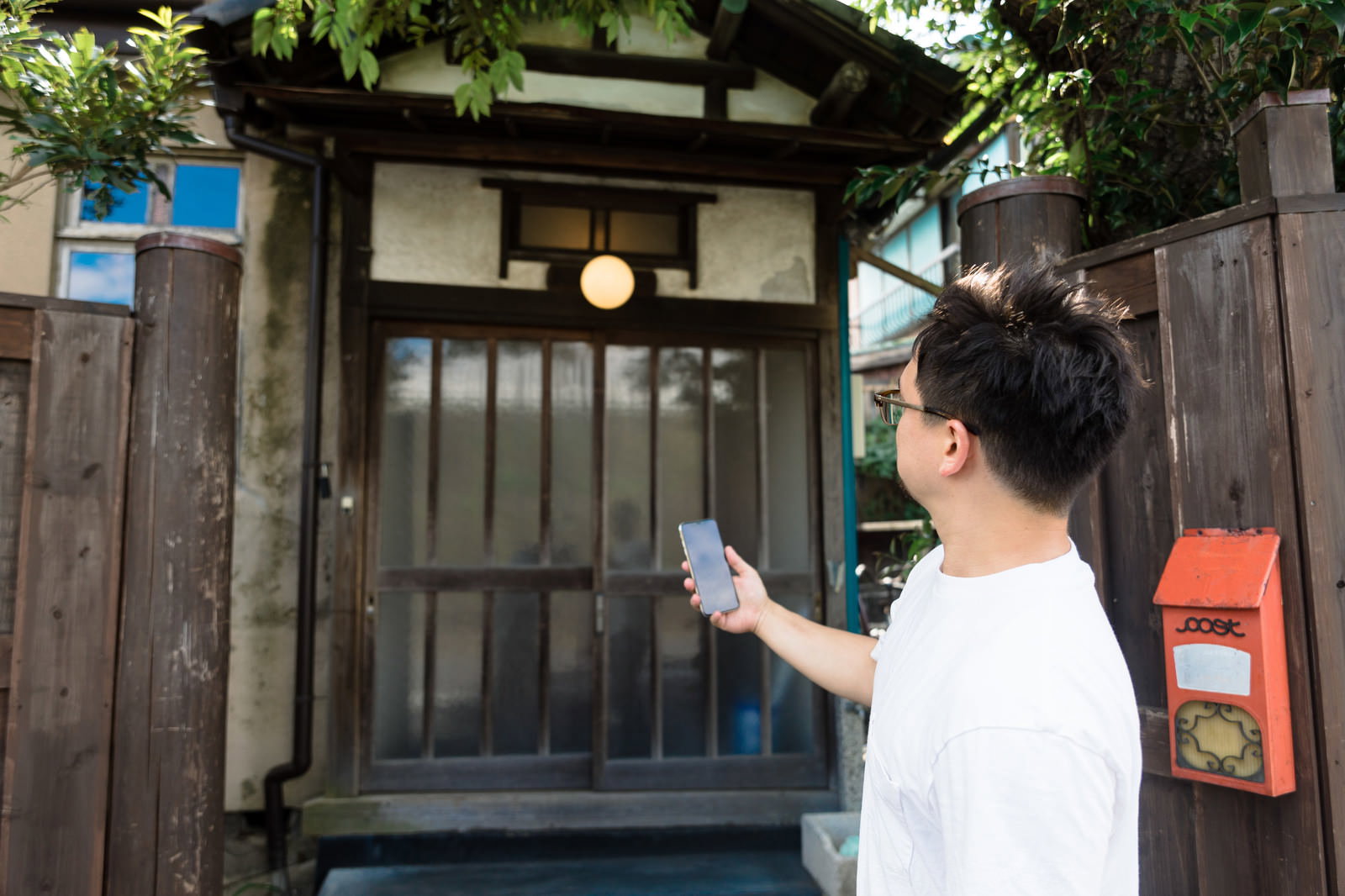 スマートフォンを持ち古民家の前に立つ外国人観光客の男性［モデル：Max_Ezaki］