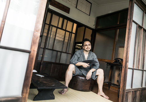 古民家の縁側で甚平姿の外国人男性が扇子を持って涼む