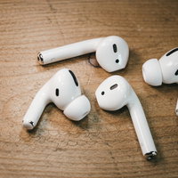 木目のテーブルに散らばるAirPodsとAirPods Proの充電ケースの写真