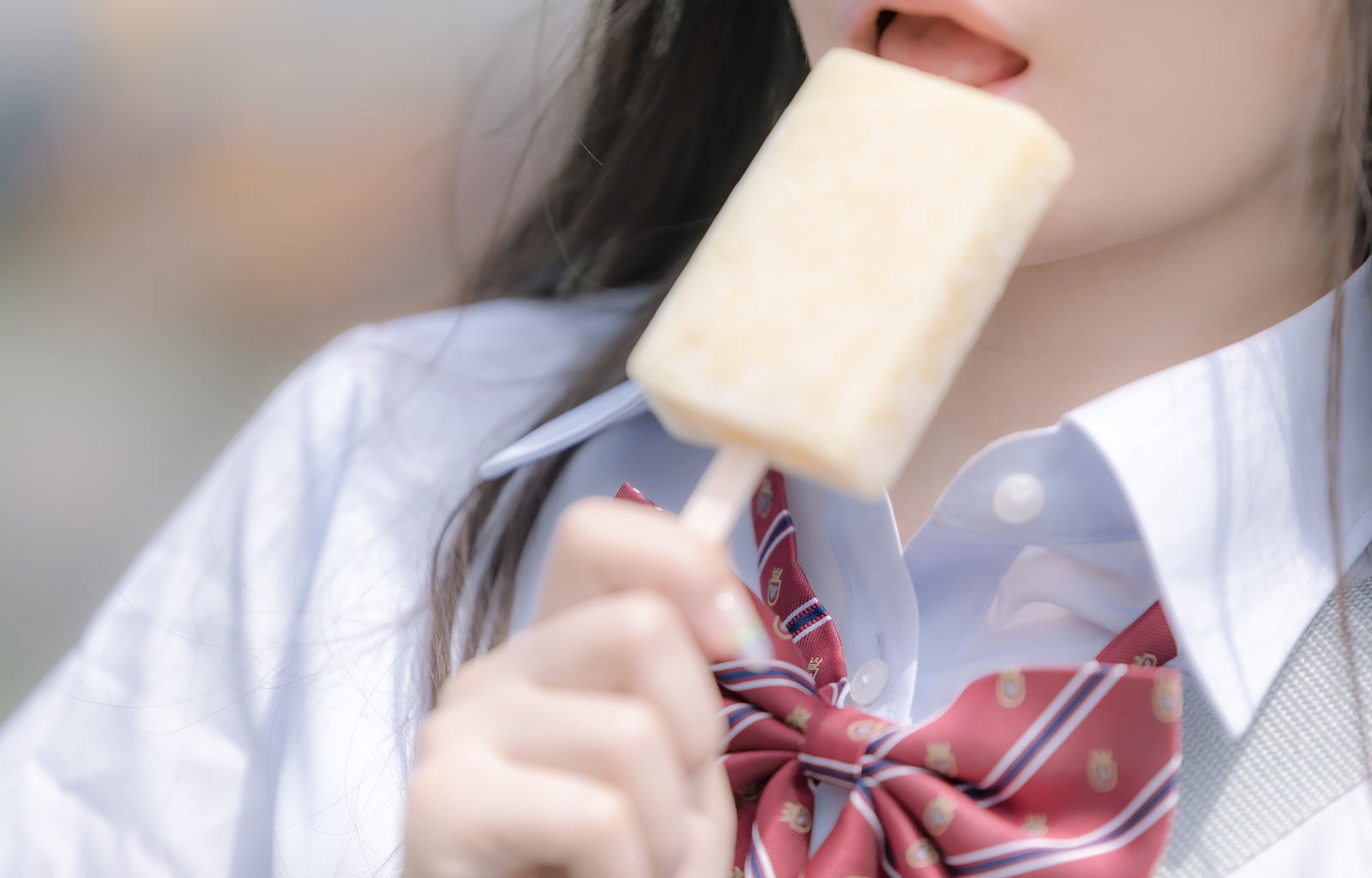 白いアイスキャンディーを食べる女子高生の口元アップ［モデル：石投げて美奈代］