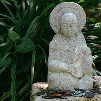 小さな石仏の足元の置かれたお賽銭の写真