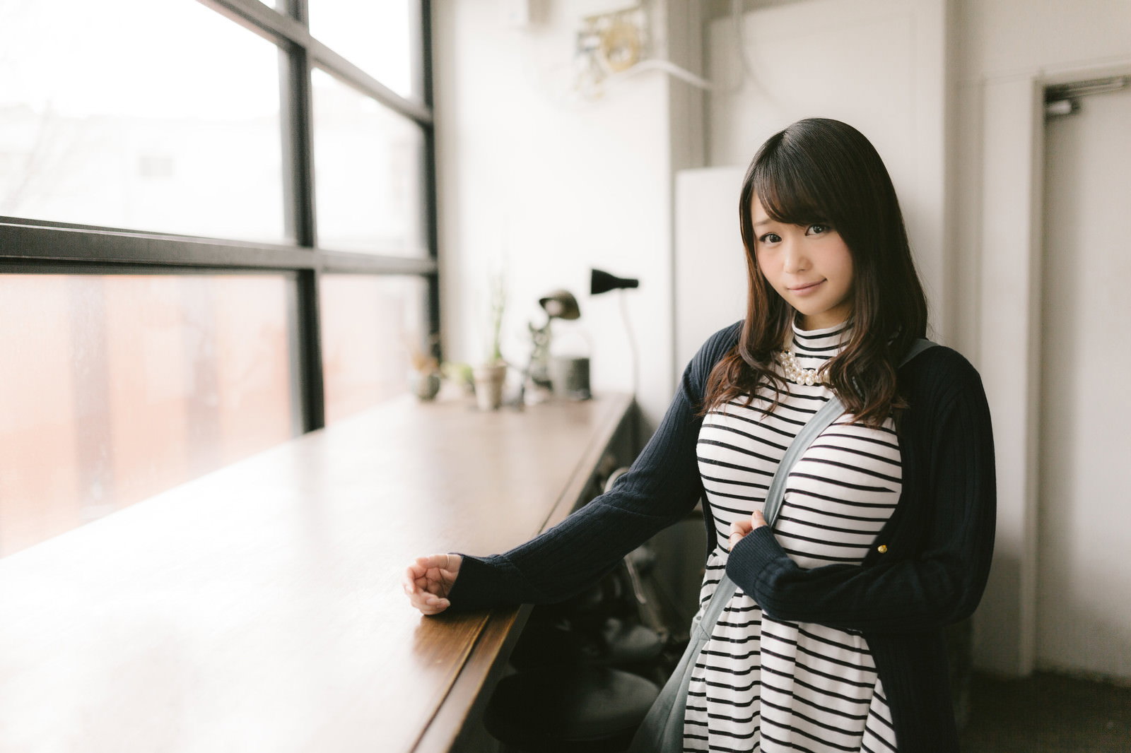 カフェの窓際でカウンターに手を置いて立つ女性［モデル：茜さや］