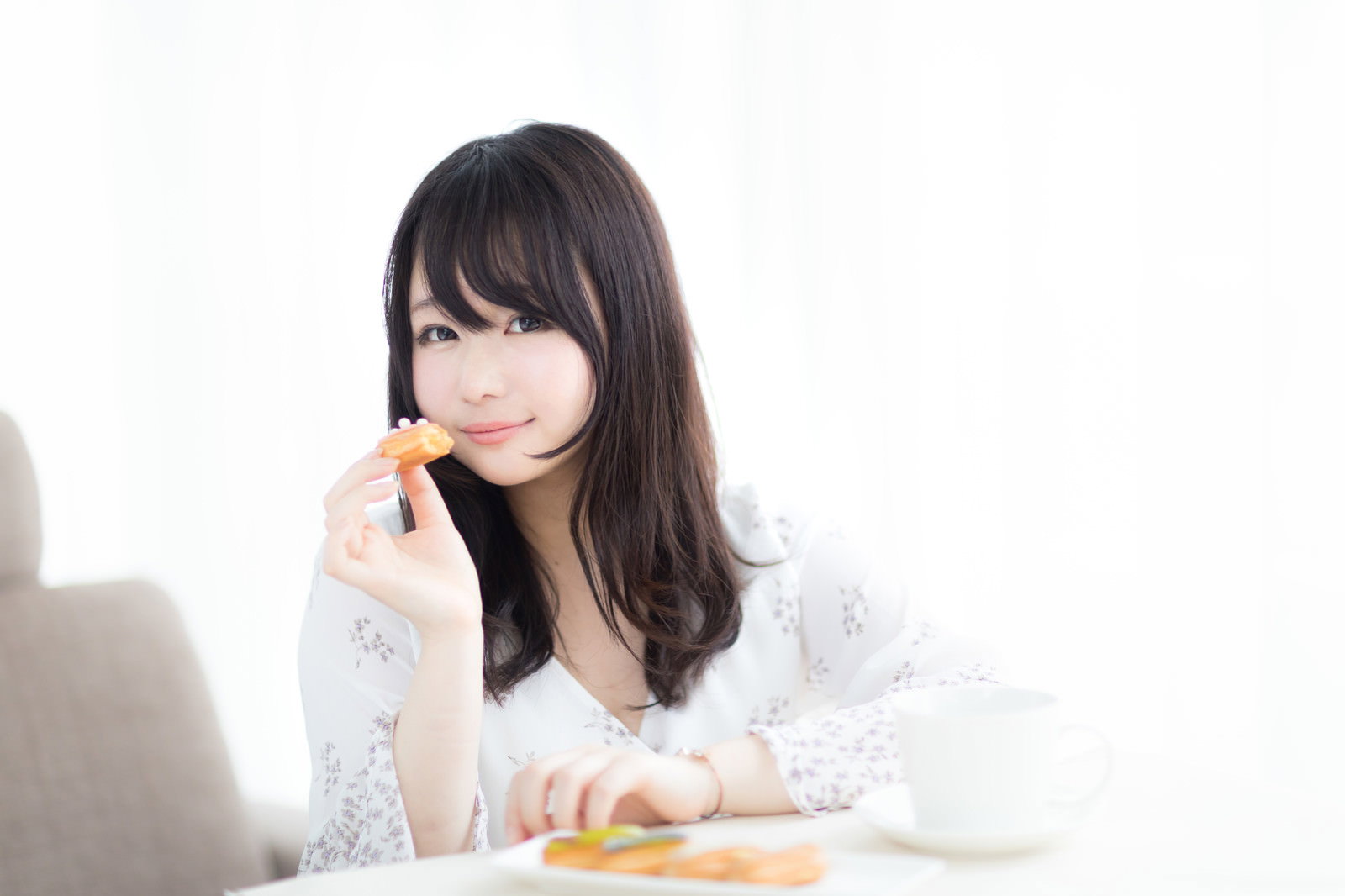 白い服を着た女性がエクレアを手に持ち食べている［モデル：茜さや］