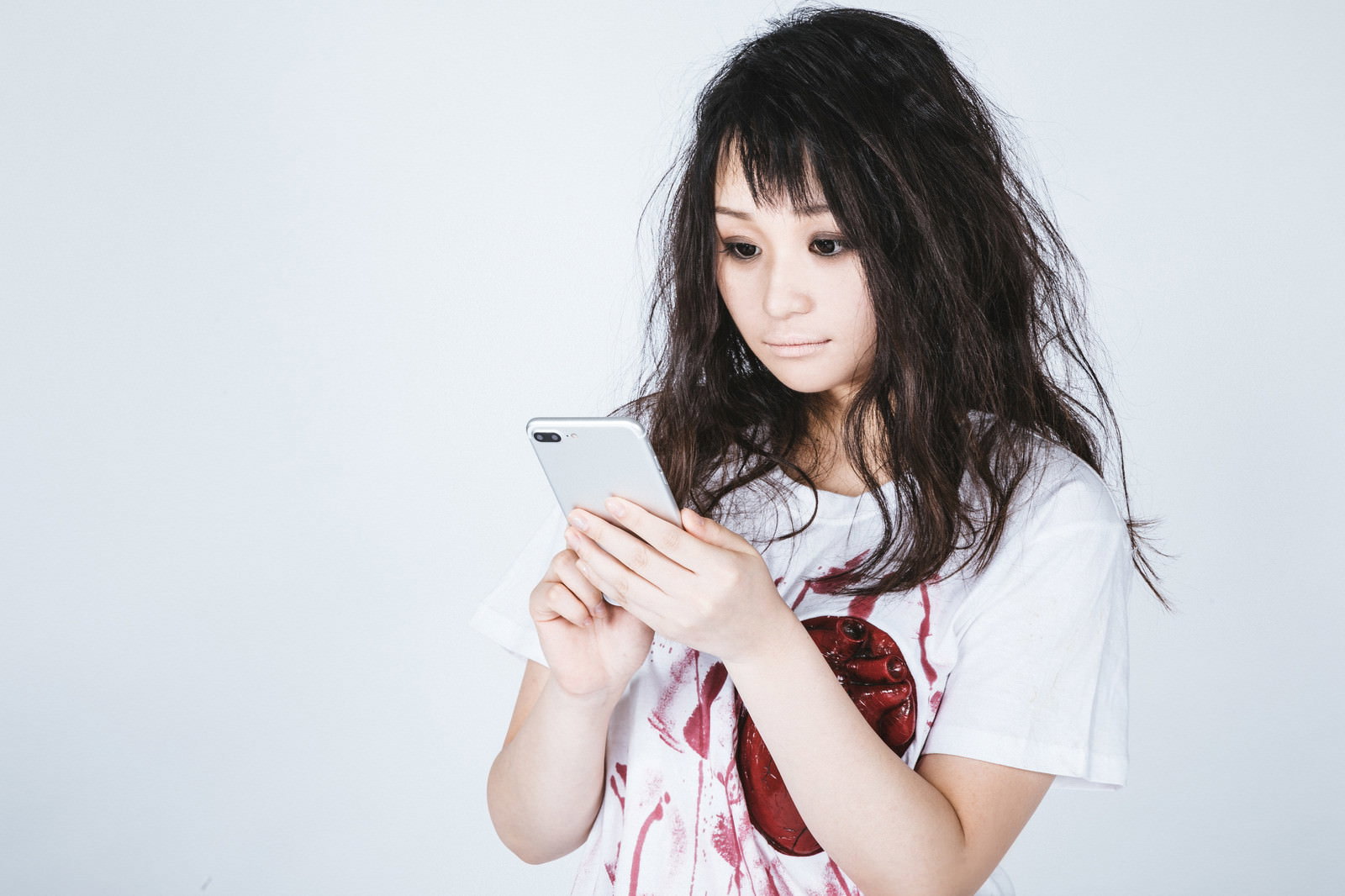 具合が悪い風メイクでスマートフォンを持つ白いシャツの女性［モデル：茜さや］