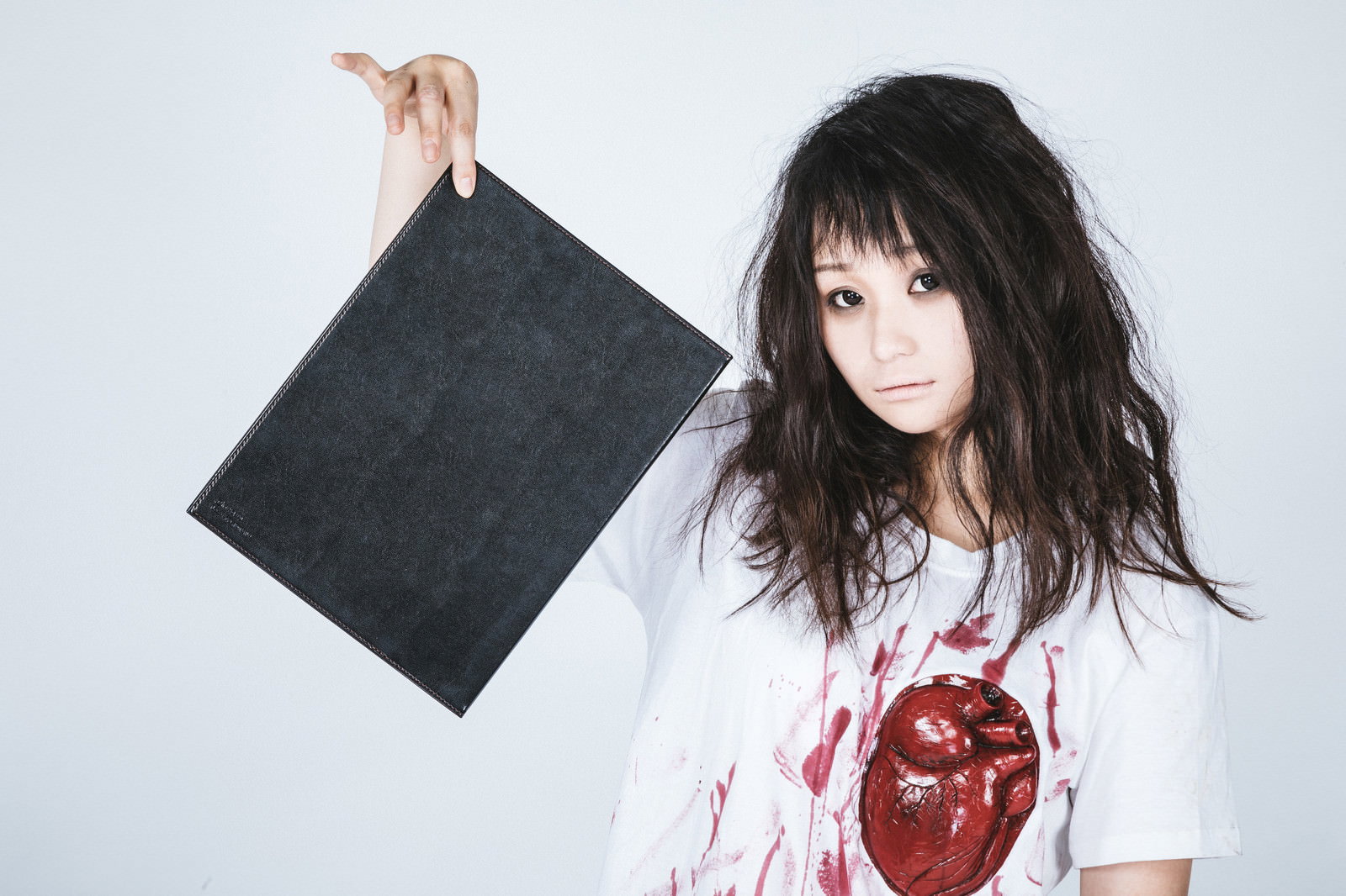 黒いノートを片手で持ち上げる白い衣装の女性［モデル：茜さや］