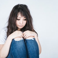 膝を抱えてうなだれる女性の体育座り｜メンタルヘルスの写真