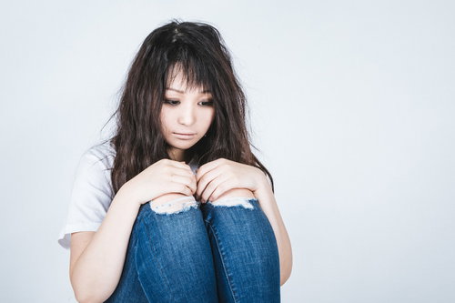 膝を抱えてうなだれる女性の体育座り｜メンタルヘルス