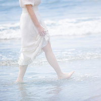 岩井海岸の波打ち際を裸足で歩く白いワンピースの女性の写真