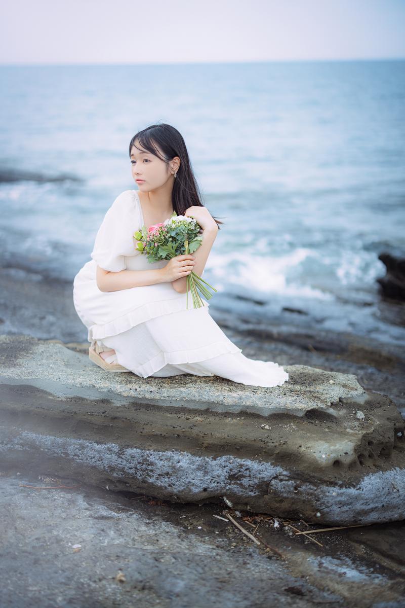 岩礁に座り花束を抱える女性［モデル：茜さや］