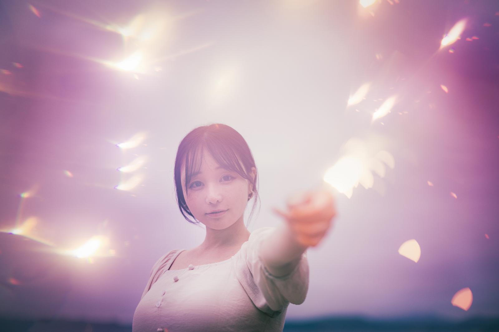 白いシャツを着た女性が手持ち花火を持ち、火花が輝いている［モデル：茜さや］