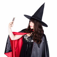 スマートフォンで自撮りする魔女のハロウィンコスプレの写真