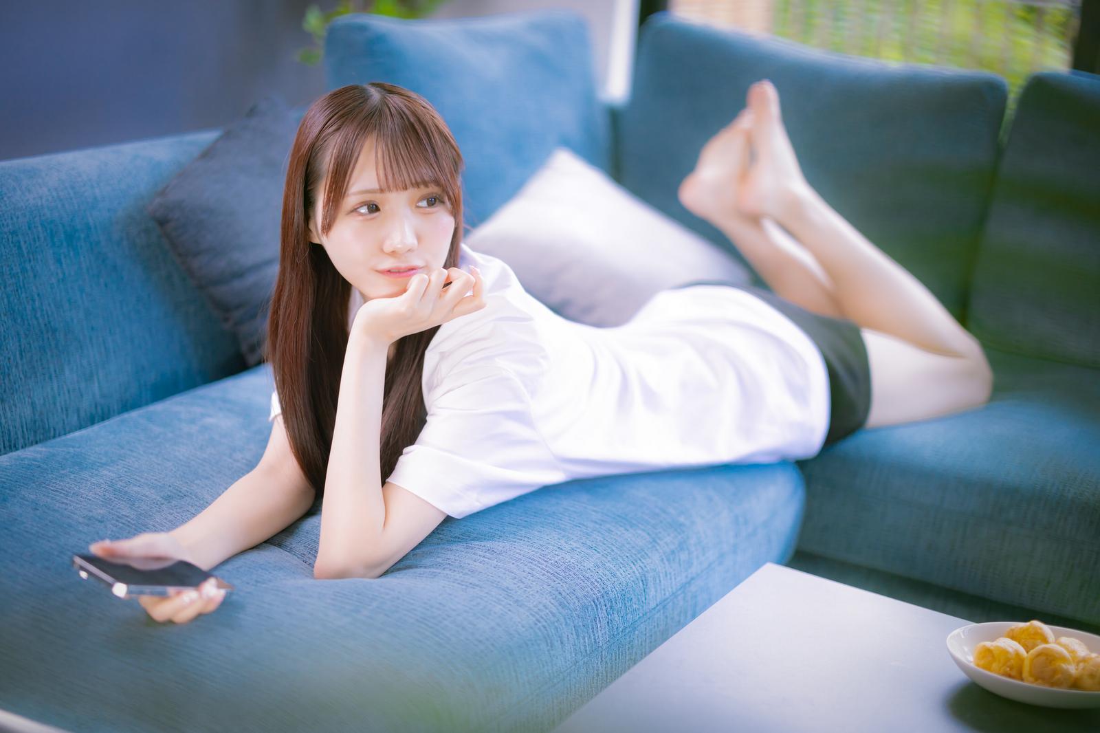 ソファーで横たわってスマートフォンを見る女性［モデル：あき］