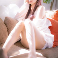 朝の陽だまりの中、ソファーに座る白いシャツの女性の写真