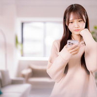 スマホを持って考える女性が過ごす柔らかな光の室内の写真