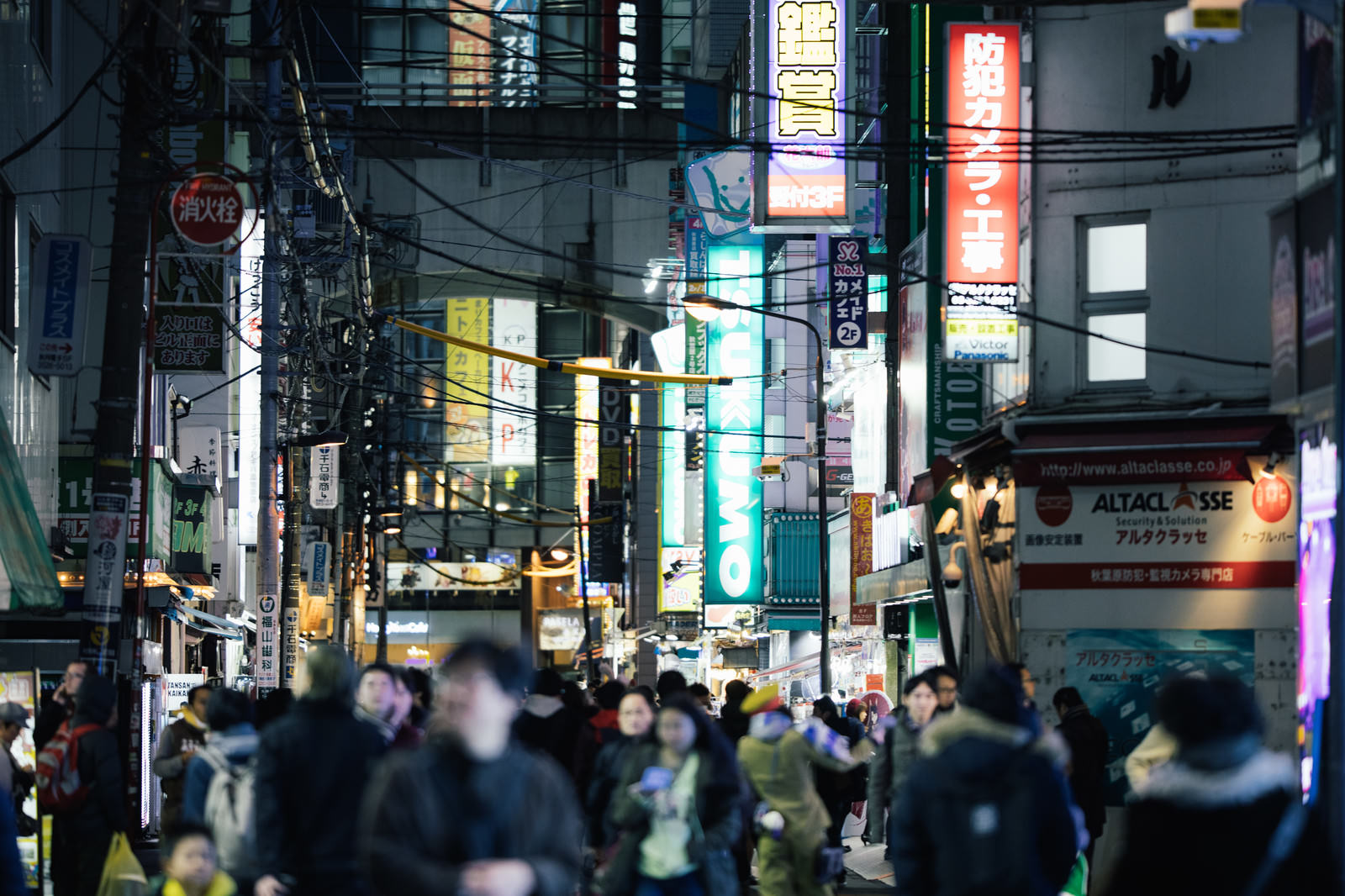 夜の秋葉原の路地裏でネオン看板が光る中、多くの通行人が行き交う人混みの風景