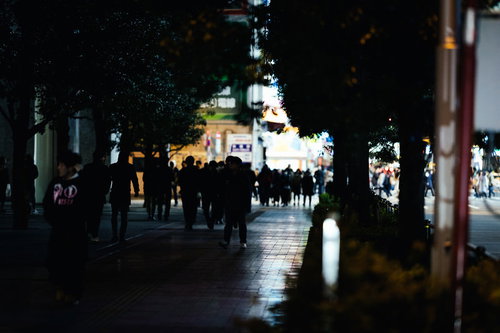 帰宅時間に駅前の歩道へ歩く通行人達の夜間風景