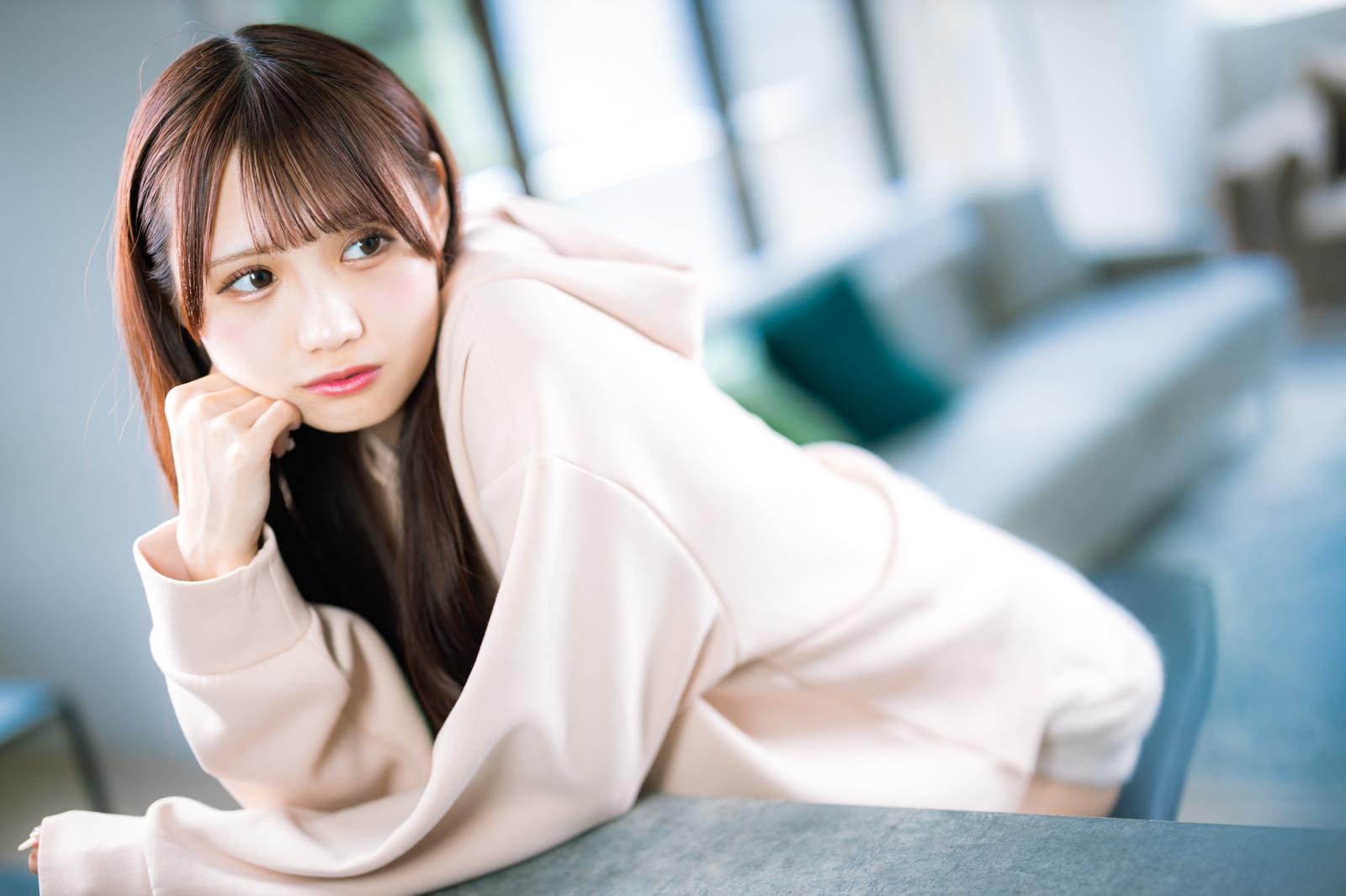 ベージュのシャツを着た女性が頬杖をついて迷いながら考えている［モデル：あき］