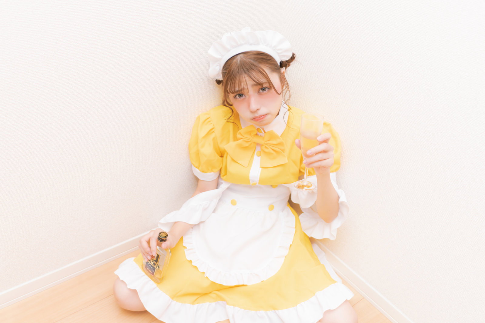 黄色いメイド服を着た女性が床に座り、頭を抱えて困った表情を見せている［モデル：高尾実生］