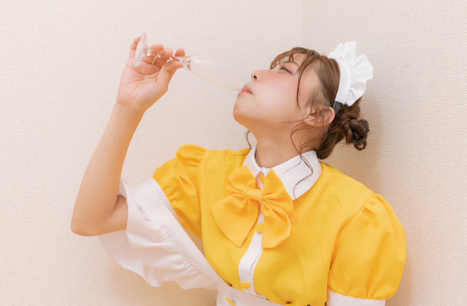 黄色いメイド服を着た女性がシャンパングラスを口に運んで飲んでいる様子［モデル：高尾実生］