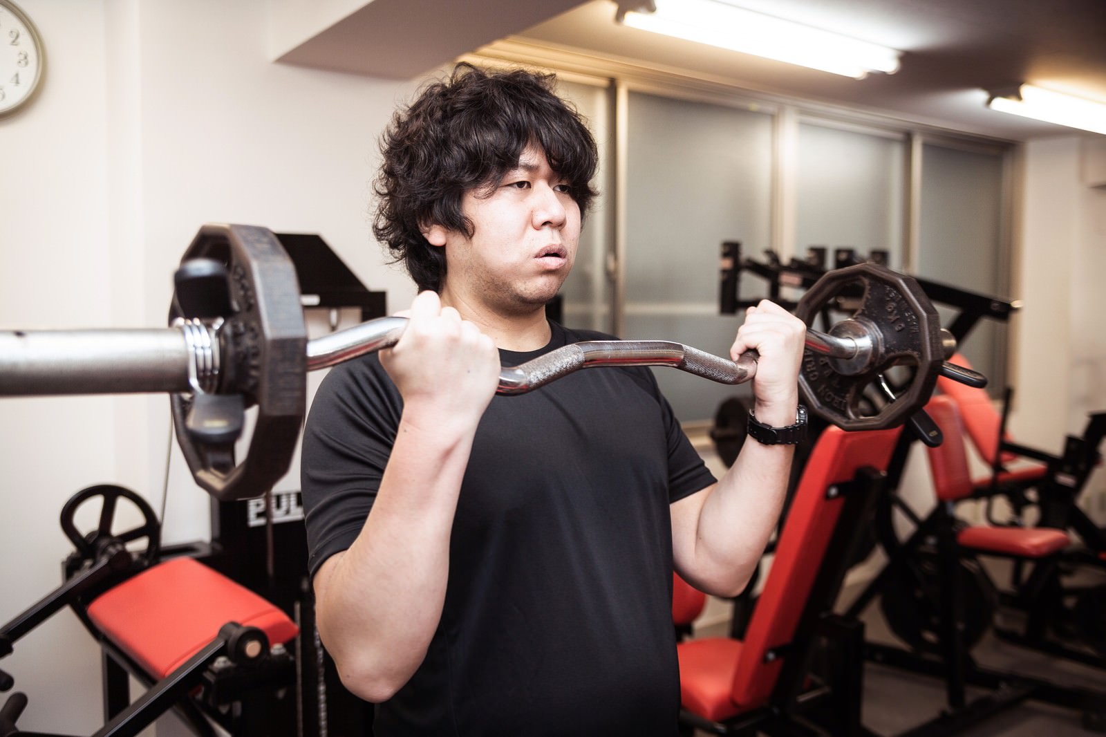 スポーツジムでEZバーでカール動作をしている男性［モデル：あまのじゃく］