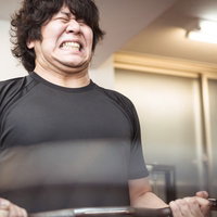 バーベルカールで顔をゆがめる男性の筋トレ姿の写真