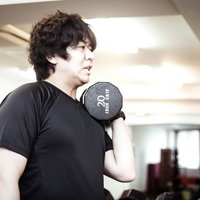 スポーツジムでダンベルカールを行う男性のトレーニングの写真