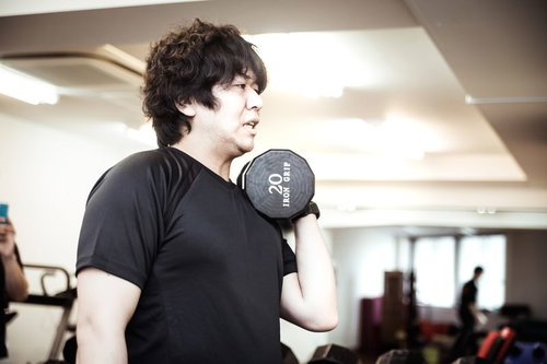 スポーツジムでダンベルカールを行う男性のトレーニング