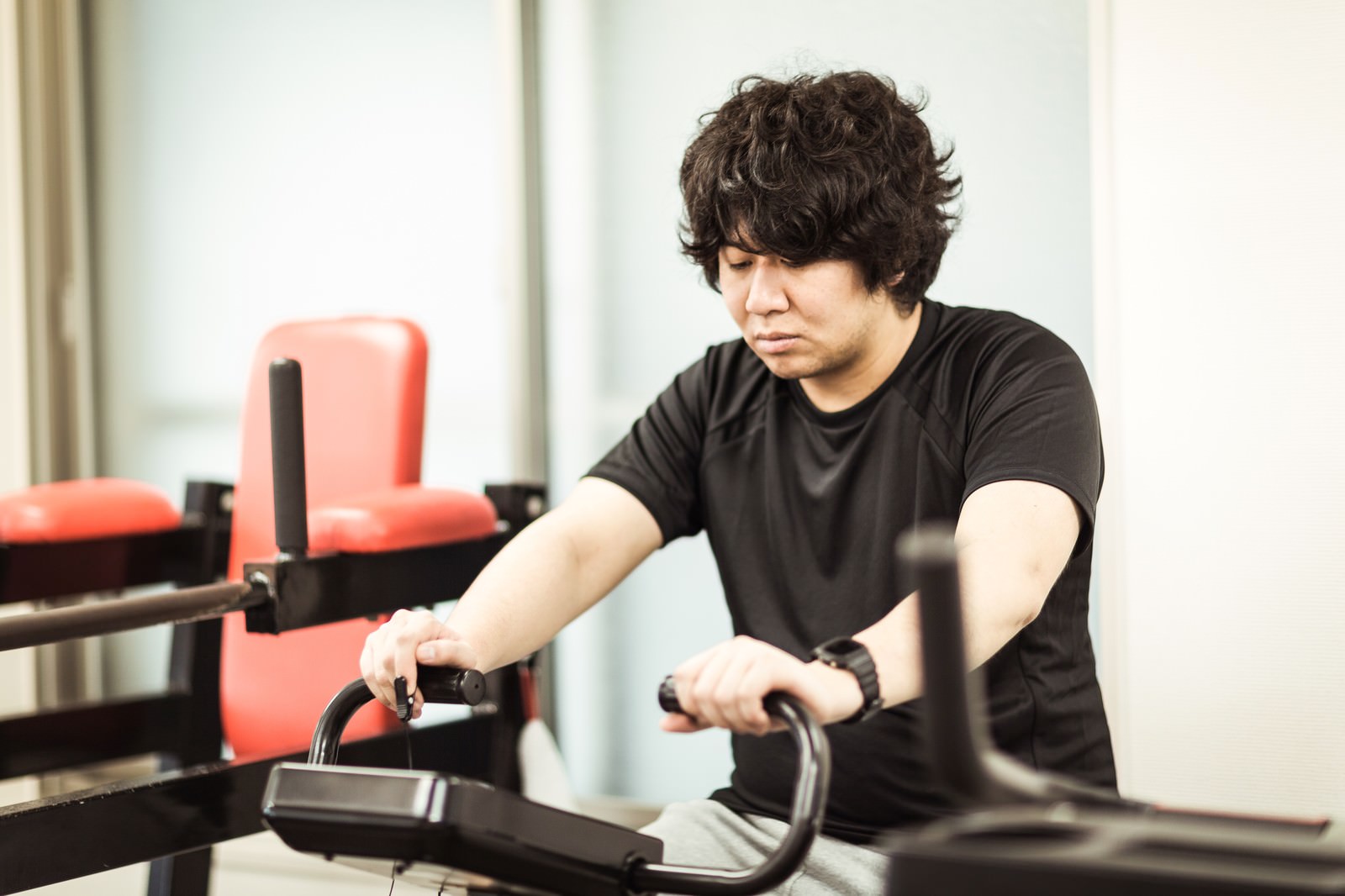 スポーツジムでエアロバイクに乗りながら心拍数を確認する男性［モデル：あまのじゃく］