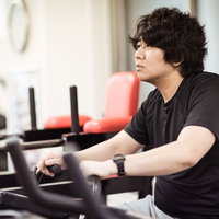 夕方のニュース番組をエアロバイクでチェックする男性の写真